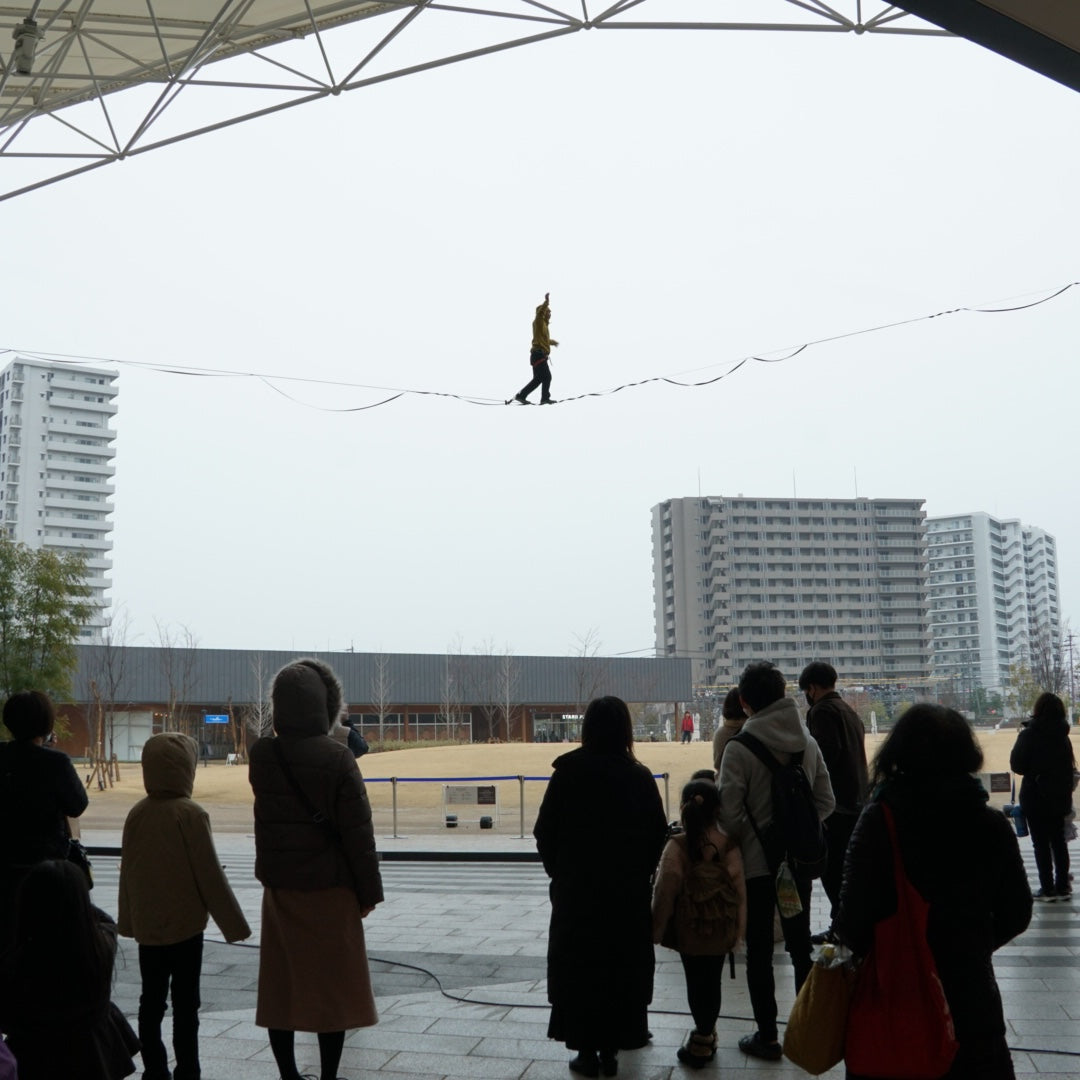屋外の広場でスラックライン高所デモを披露する選手と観客。Slackline Researchのイベント実績紹介用写真。